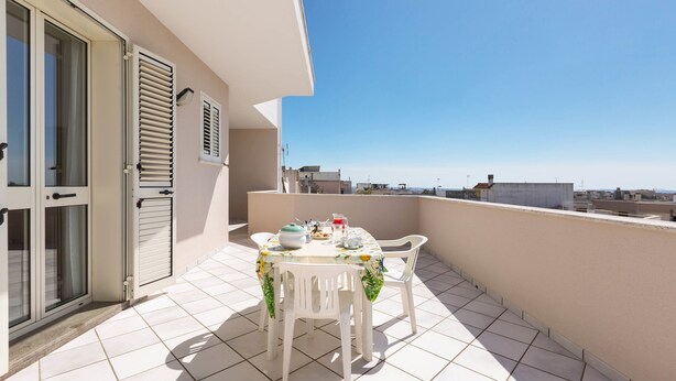 Ein Balkon mit Tisch für zwei Personen, einer Glastür und Blick auf die Stadt.