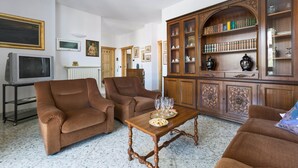 Ein Wohnzimmer mit braunen Polstermöbeln, einem Holzschrank mit Glastüren und einem Fernseher auf einem Standfuß.