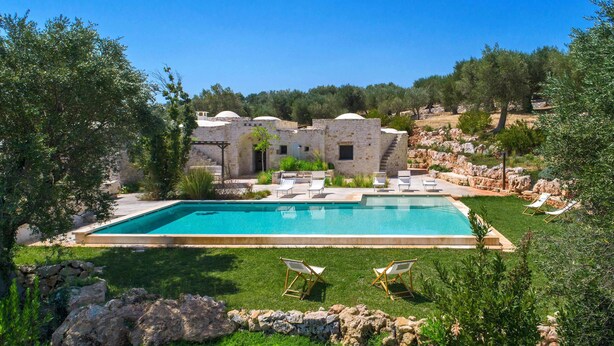A pool with lounge chairs, a stone building, and a grassy area with trees. - La Dialma (Ostuni)