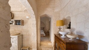 A rustic room with a stone wall, wooden furniture, and a bed in the background. - La Dialma (Ostuni)