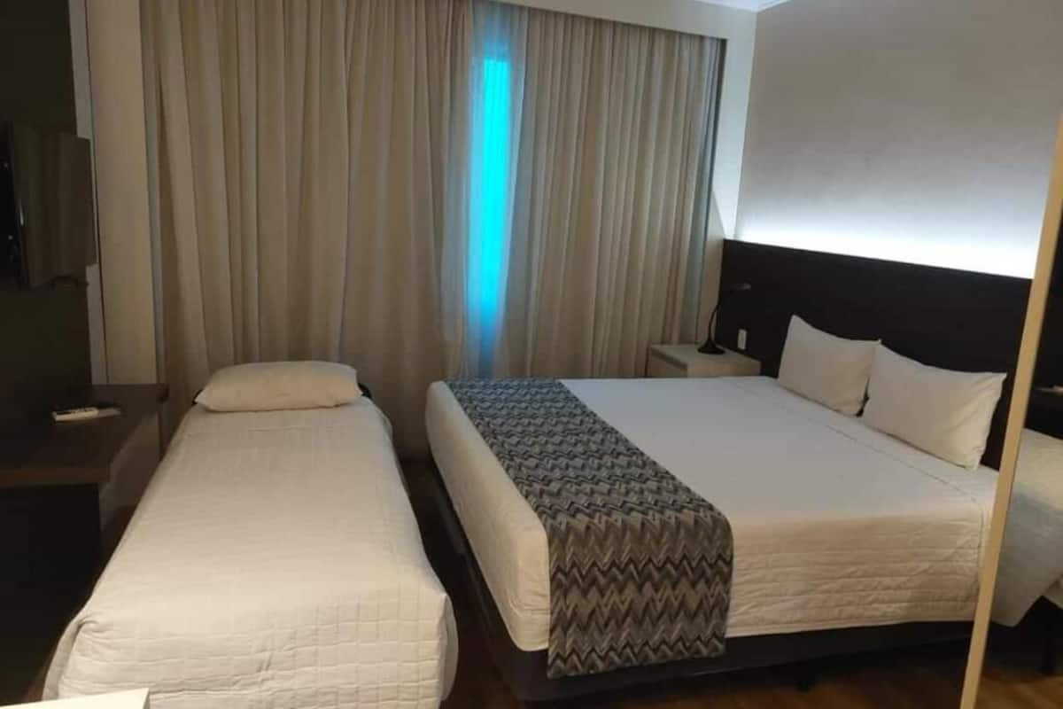 Ein Hotelzimmer mit zwei Betten, einem Nachttisch und einem großen Fenster mit Vorhängen.