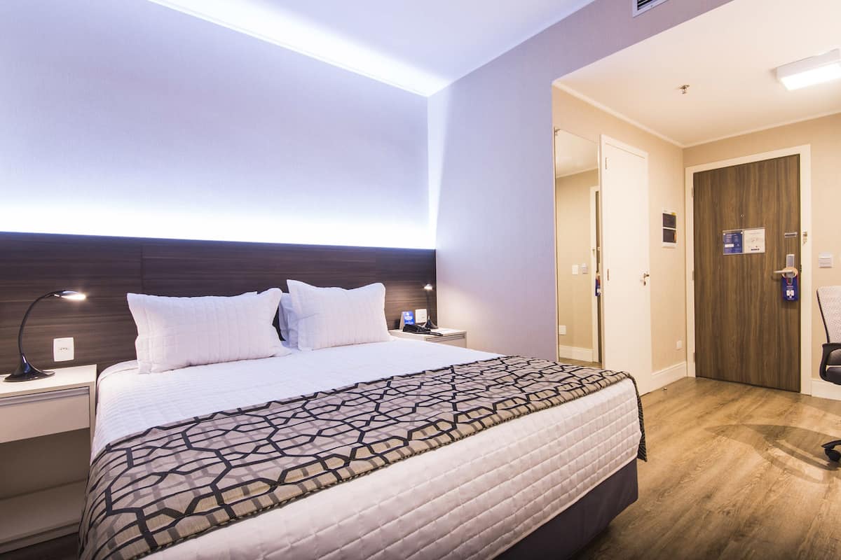 Ein Hotelzimmer mit einem großen Bett, Nachttischen, einem Schreibtisch und einem Kleiderschrank.