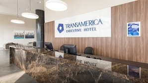 Een receptiebalie bij het Transamerica Executive Hotel met een marmeren aanrecht, moderne verlichting en een groot bord erboven.