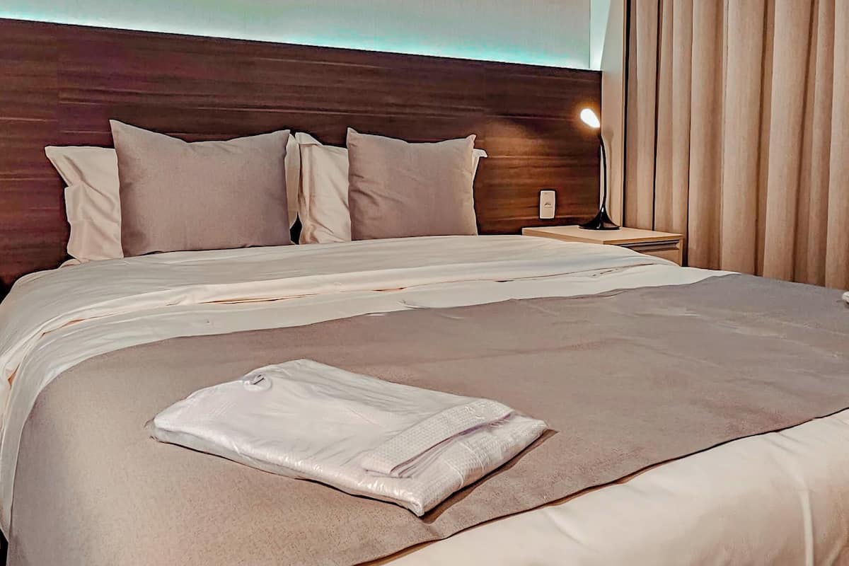 Ein Hotelzimmer mit einem großen Bett, einem hölzernen Kopfteil, einem Nachttisch mit Lampe und einem Fenster mit Vorhängen.