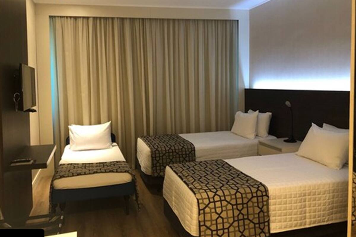 Ein Hotelzimmer mit zwei Einzelbetten, einem Schreibtisch mit Stuhl, einem Fernseher und einem großen Fenster mit Vorhängen.