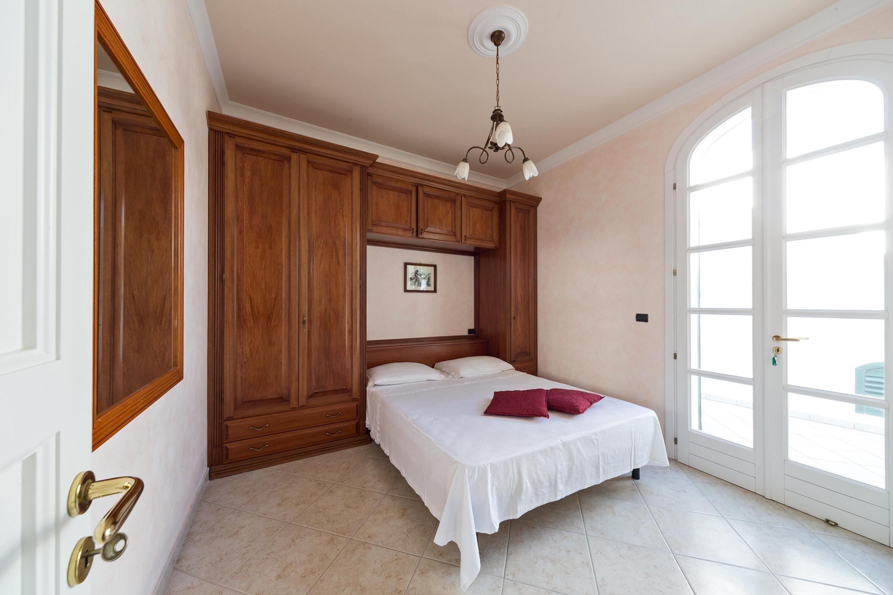 Un dormitorio con una cama, armarios de madera, una puerta blanca y un ventanal grande.