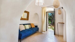 A modern interior with a blue sofa, a hanging light fixture, and a view through an archway. - Le Ali Bianche (Ostuni)