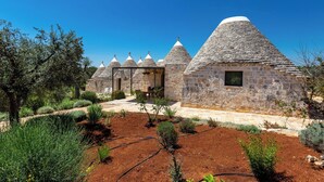 A row of stone-roofed buildings with a garden in the foreground. - Le Ali Bianche (Ostuni)