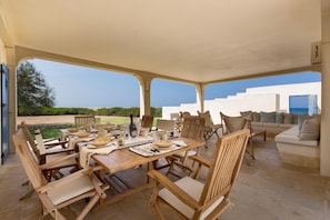 Eine Terrasse im Freien mit einem Holztisch, der für das Essen gedeckt ist, umgeben von Holzstühlen und einer Couch.