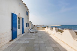 Eine Seeterrasse mit weißen Liegestühlen und blauen Fensterläden mit Blick auf den Ozean.