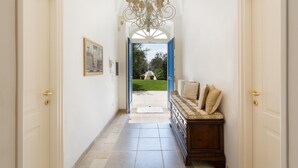 A hallway with a chandelier, a bench with cushions, and a door leading outside. - Lo Scoglio Bianco (Ostuni)