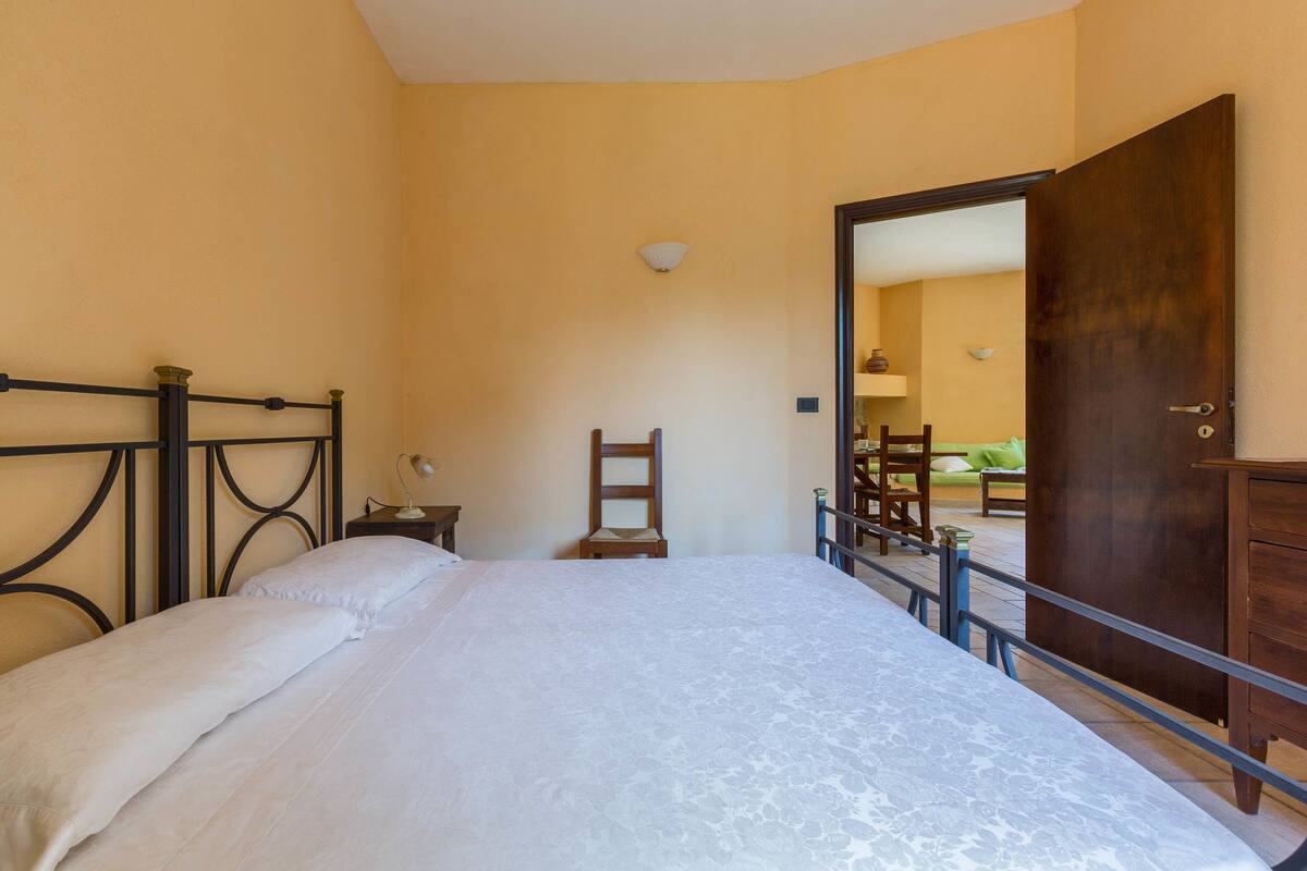 Un dormitorio con cama, una silla, un aparador de madera y una puerta que da a otra habitación.