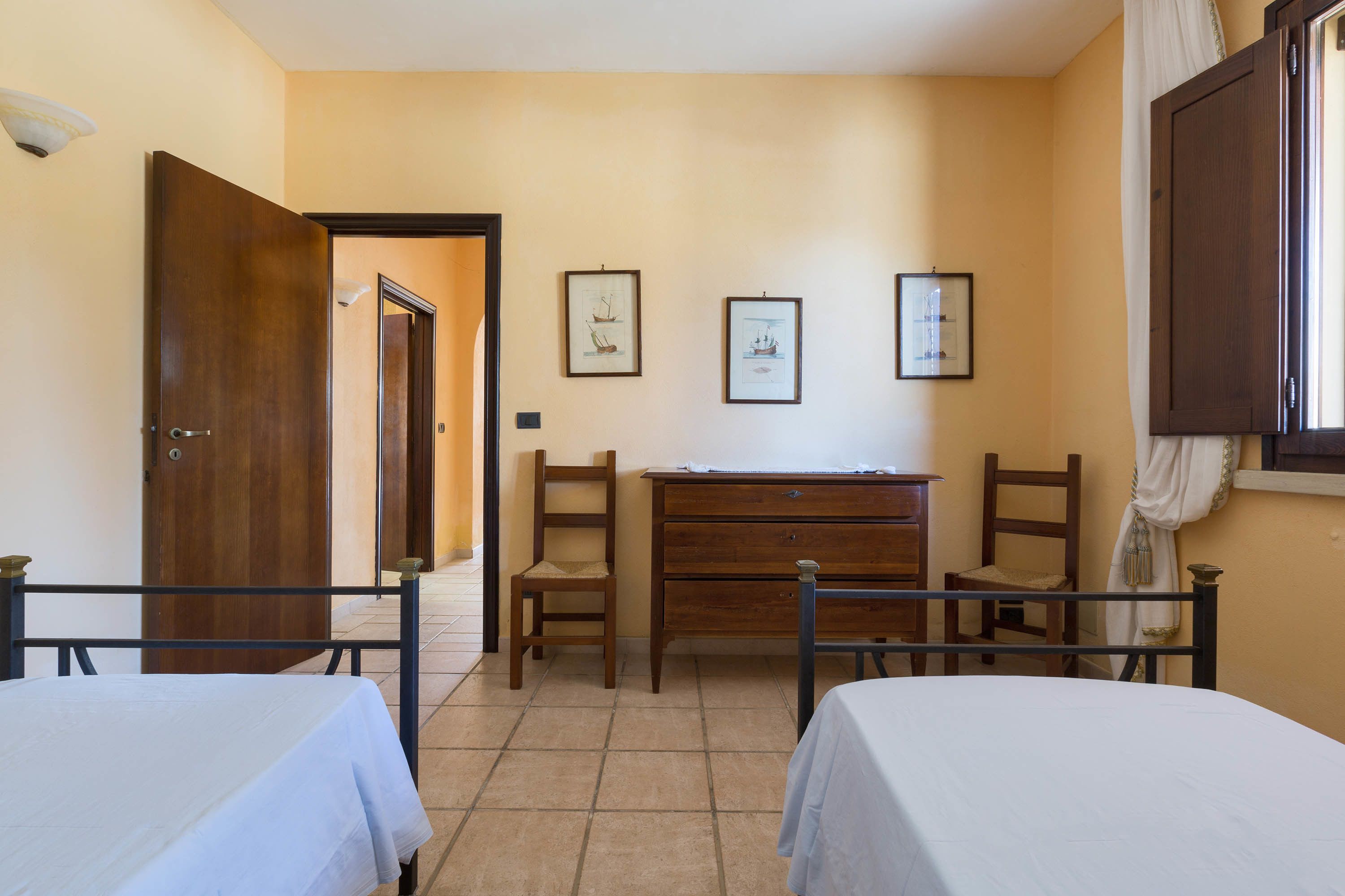 A room with two beds, a wooden dresser, and three framed pictures on the wall.