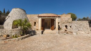 Un edificio de piedra con techo de tejas, una estructura circular a la izquierda y un acceso a un espacio interior.