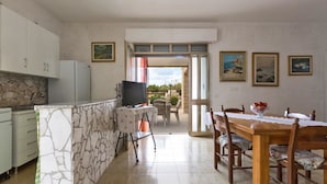 A kitchen with a stone island, a dining table with chairs, and a TV on a stand. - 937 Riva del Conte by Barbarhouse (Porto Cesareo)
