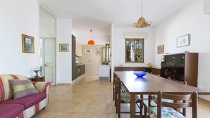 Amplia sala de estar con sofá, mesa de comedor y sillas. Cuenta con una zona de cocina con armarios y refrigerador.