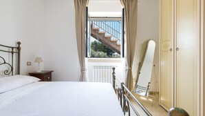 Une chambre à coucher comprenant un lit, une table de chevet, une lampe, une fenêtre avec des rideaux et un miroir.