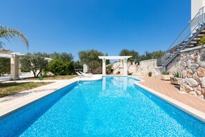 A swimming pool with a stone wall and a pergola. - Sogno d`Itria (Villa Castelli)
