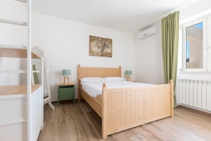 A bedroom with a wooden bed, a green nightstand, a desk, a map artwork, and a window with curtains.