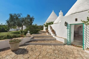 A white building with a conical roof, a stone staircase leading to a door, and potted plants. - Trulli Il Cappero (Ostuni)