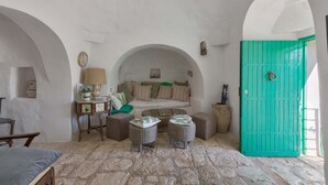 Una habitación acogedora con suelo de piedra, una puerta verde, un sofá con cojines y una pequeña mesa con una lámpara.