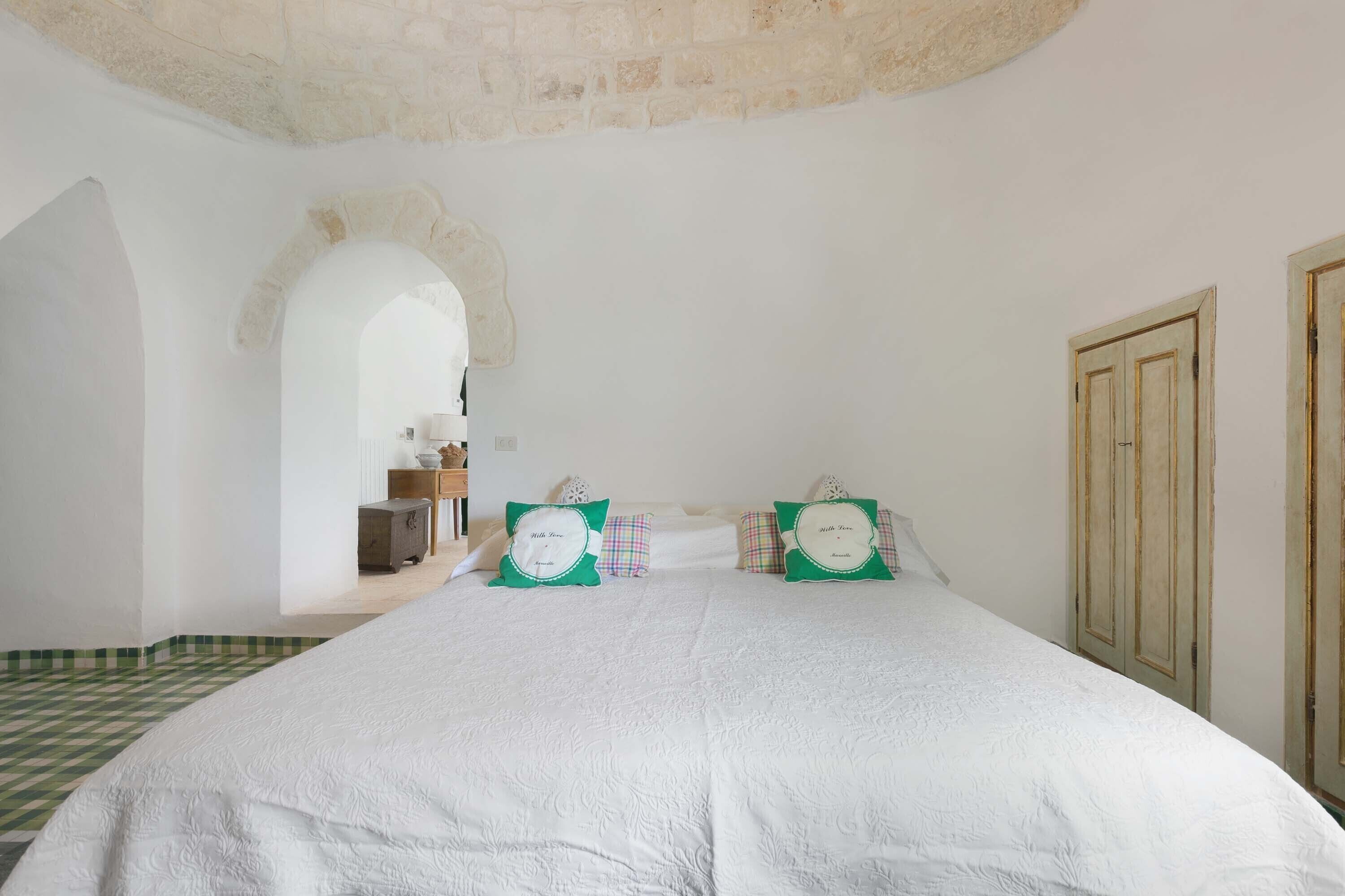 A bedroom with a large bed, two pillows, a wooden wardrobe, and an arched doorway.