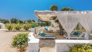A sunlit outdoor lounge area with white canopies, cushioned seating, and a stone-tiled floor. - Trulli Ion (Ostuni)