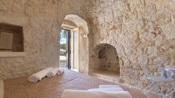 A stone-walled room with a bed, a small table, and a fireplace. - Trulli Ion (Ostuni)