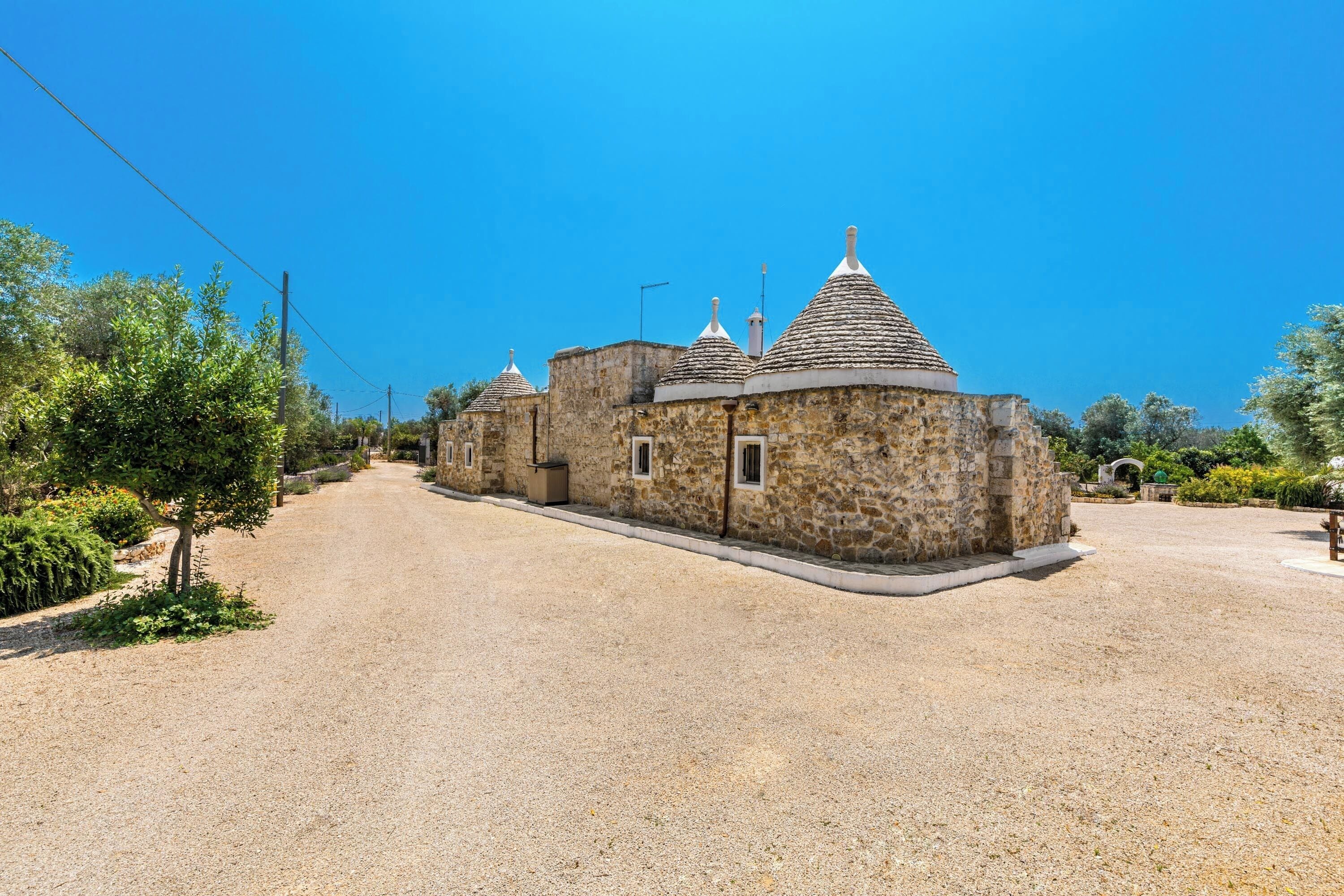 A stone building with multiple domed roofs, a gravel driveway, and surrounding greenery.