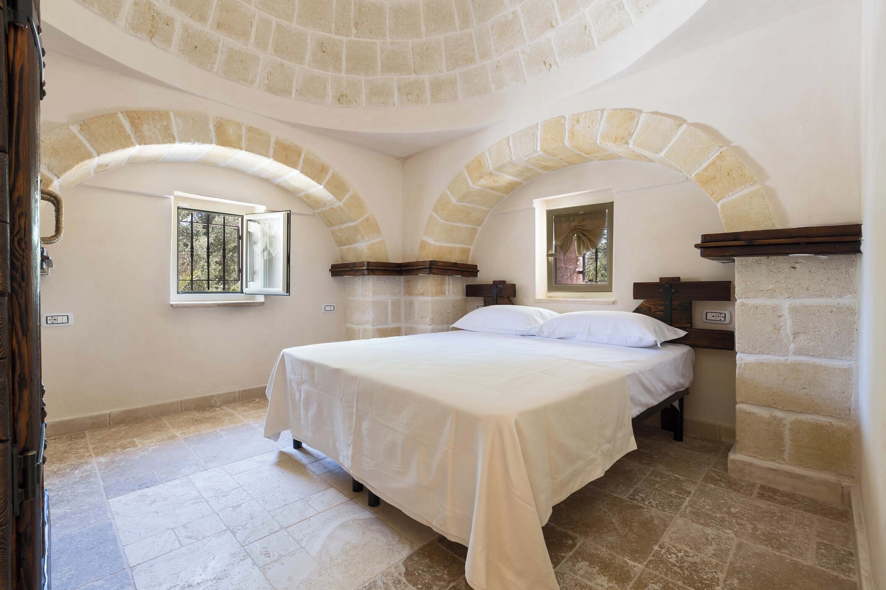 Un dormitorio con una cama grande, dos ventanas y arcos de piedra.