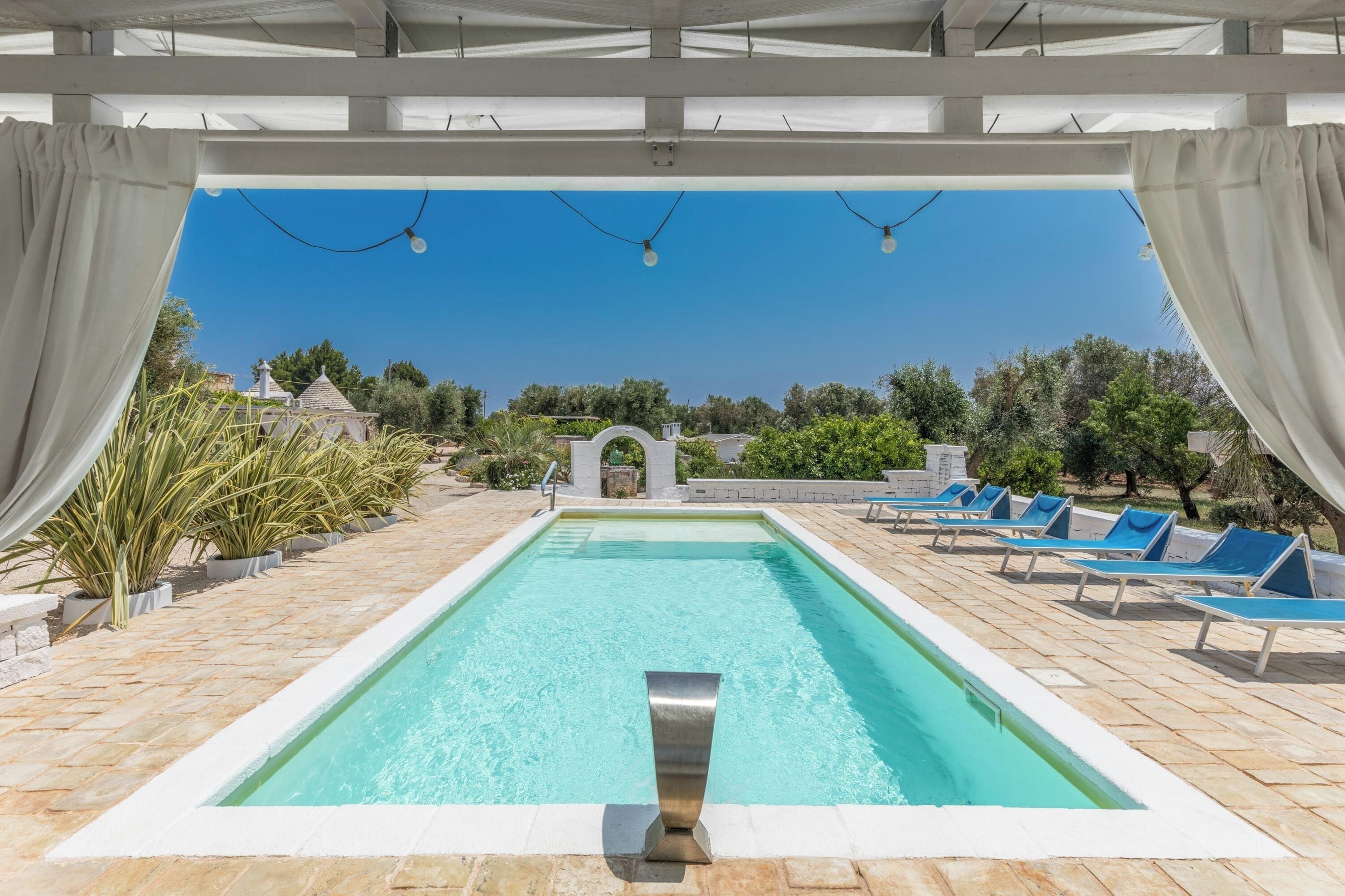 A swimming pool with a clear blue water, surrounded by lounge chairs and potted plants.