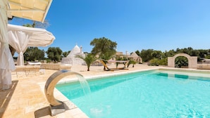 A swimming pool with a circular water feature, surrounded by stone structures and greenery. - Trulli Ion (Ostuni)