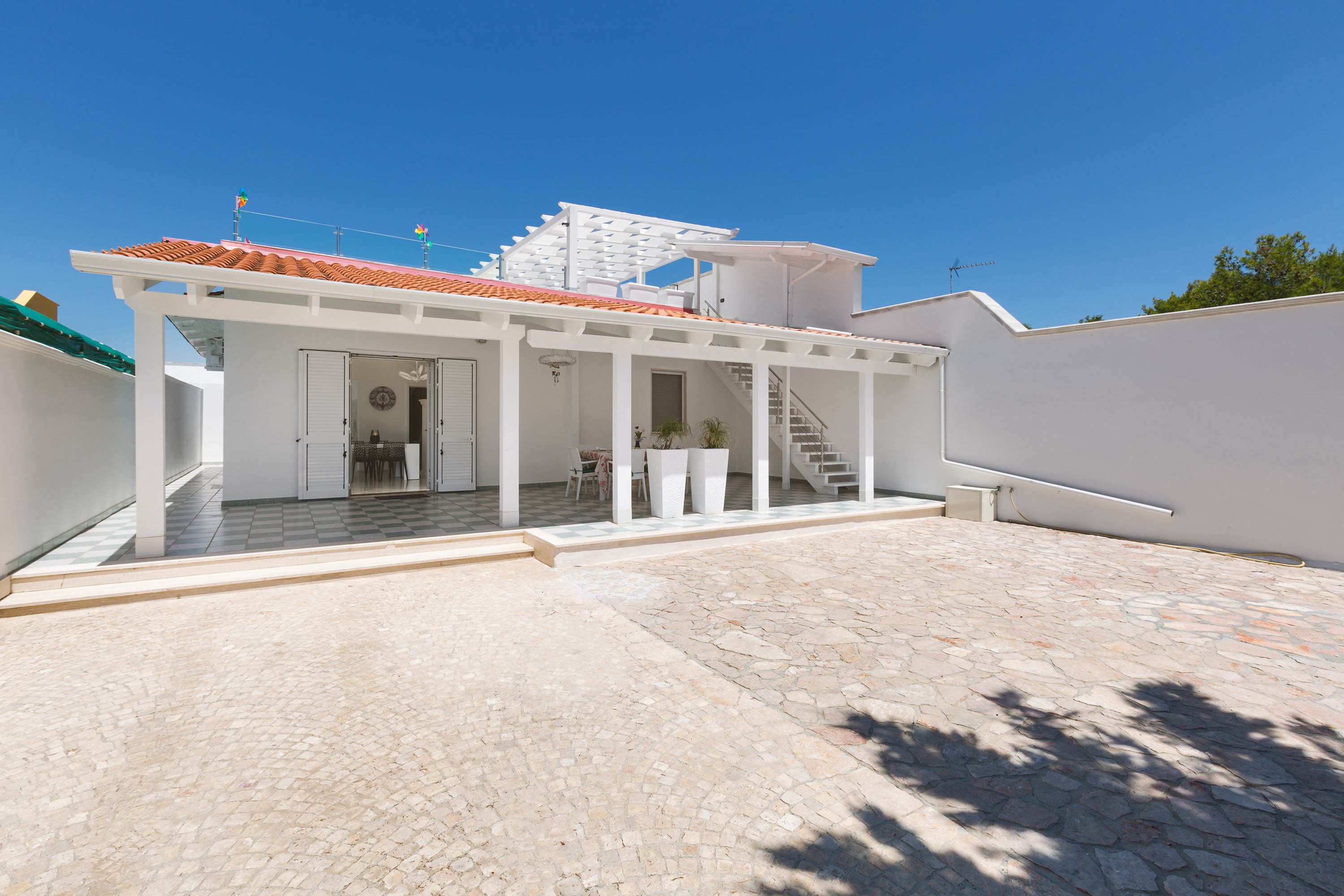 A modern house with a covered patio, a staircase leading to a second floor, and a stone-tiled courtyard.