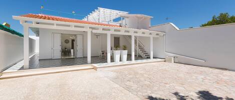 A modern house with a covered patio, a staircase leading to a second floor, and a stone-tiled courtyard.