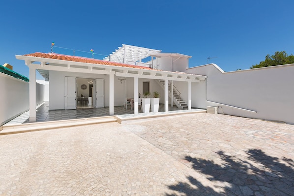 A modern house with a covered patio, a staircase leading to a second floor, and a stone-tiled courtyard.