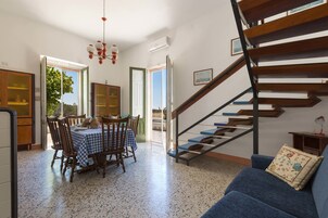Uma sala de jantar com uma mesa posta para quatro pessoas, um sofá azul, uma escada e vista para o exterior.