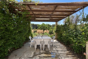 Um pátio externo com piso de azulejos hexagonais, pérgola de madeira e cadeiras brancas.