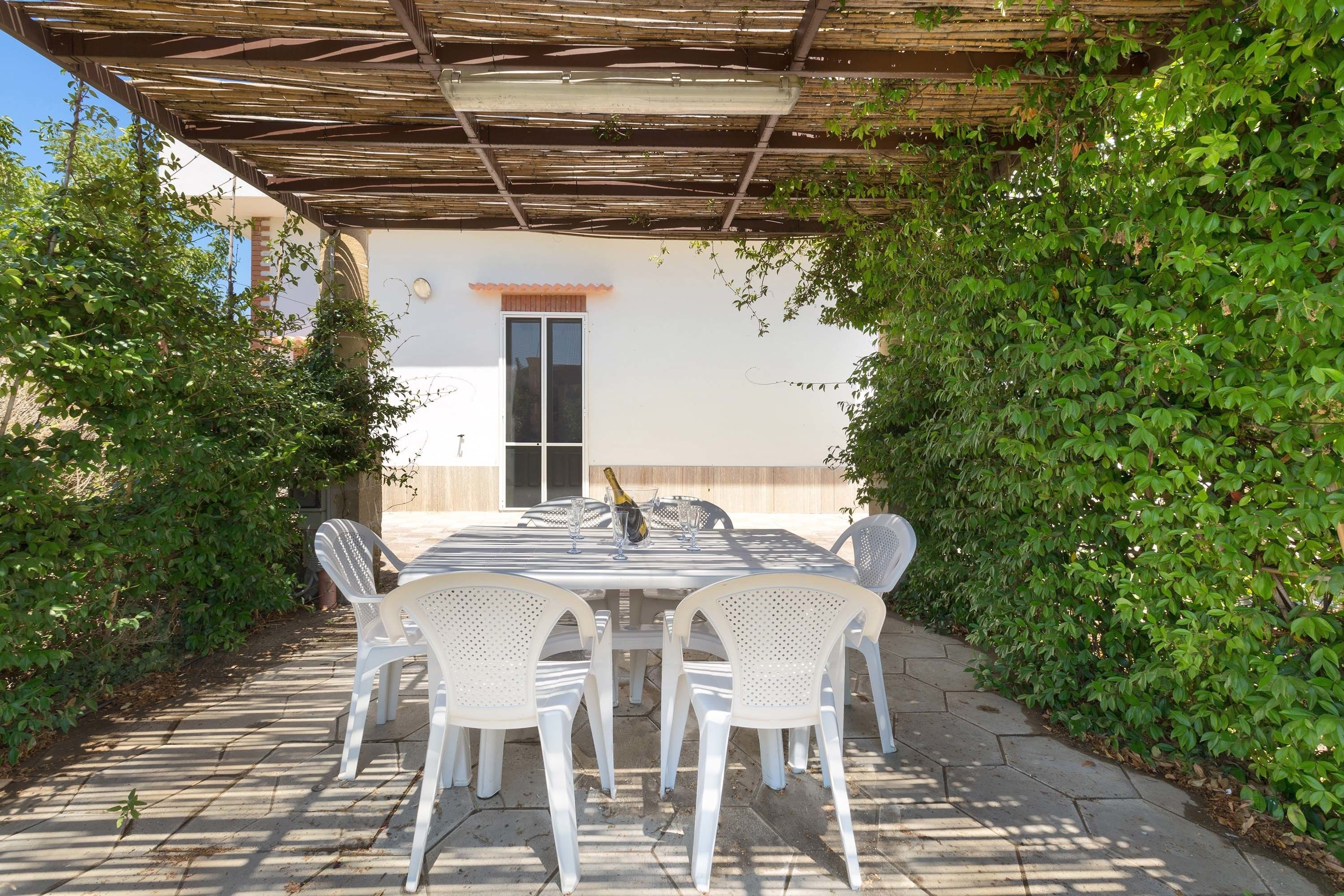An outdoor patio with a table and chairs, a bottle of champagne, and a pergola overhead.