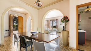 Un coin repas avec une table en bois, des chaises blanches et un grand vase rempli de fleurs rouges.