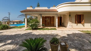 Une maison dotée d’une terrasse en pierre, d’une piscine et d’un espace extérieur couvert.