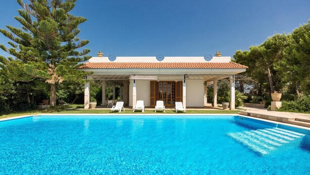 Une piscine avec des chaises longues et un pavillon abrité.