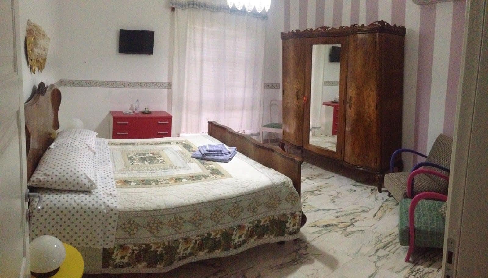 Un dormitorio con cama, armario, espejo y silla.