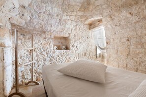 A room with a stone wall, a bed with white bedding, and a wooden ladder.