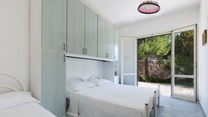 Un dormitorio con cama, armario y puerta corrediza de vidrio que da a un área exterior.