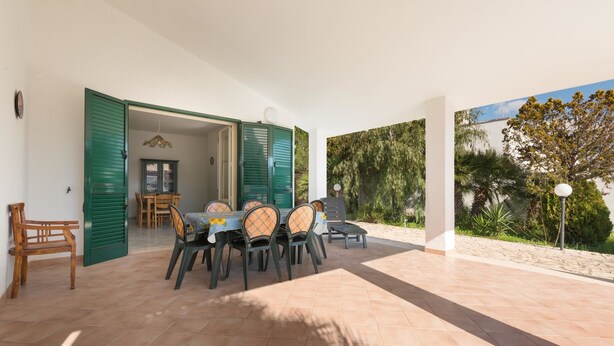 Un patio abierto con una mesa y sillas para comer, una silla de madera y una puerta verde que da a un espacio interior.