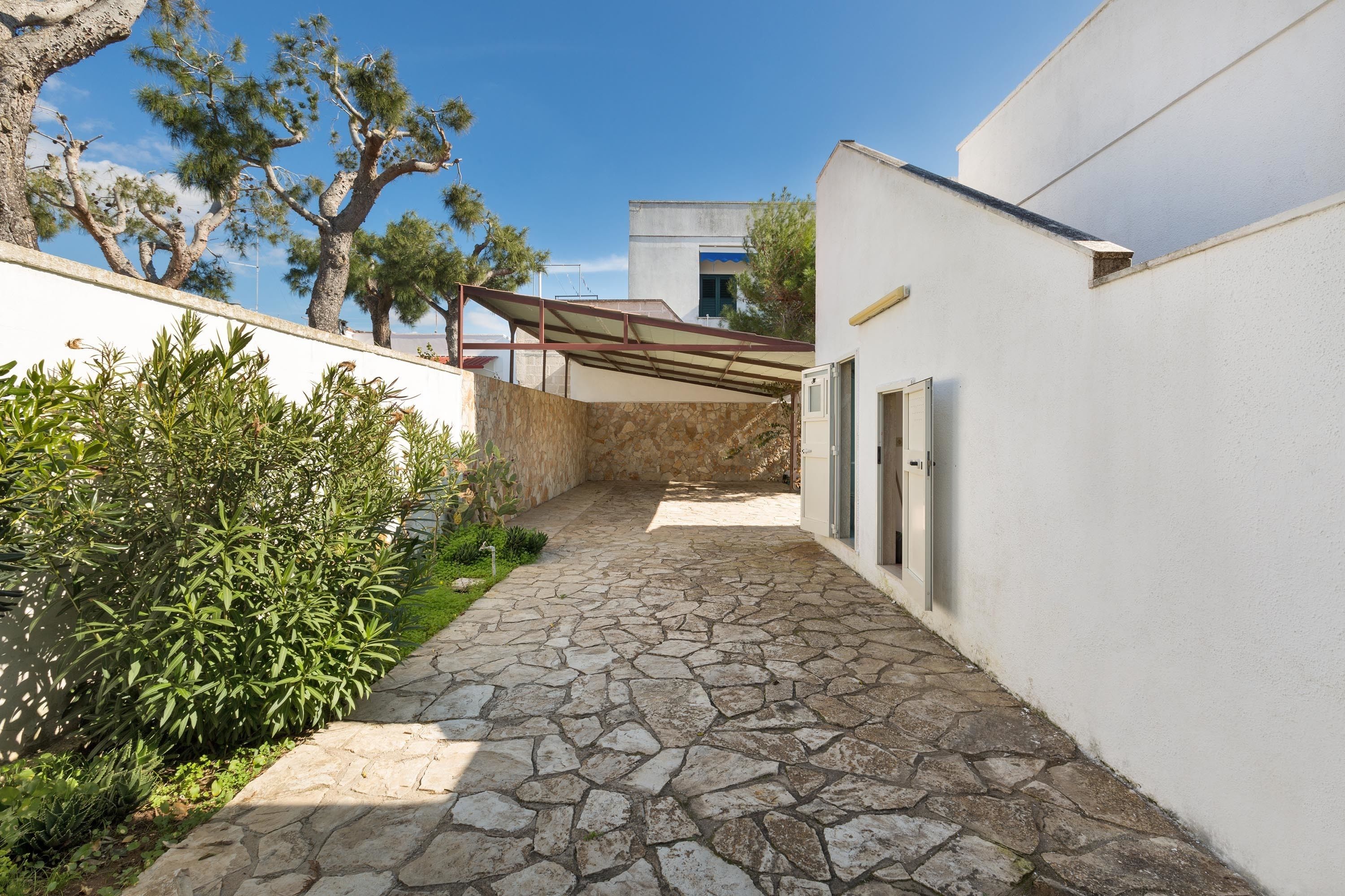 Un estrecho sendero de piedra que conduce a un edificio de fachada blanca y un espacio exterior cubierto.