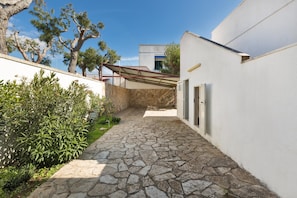 A narrow stone pathway leading to a building with a white exterior and a covered outdoor area.