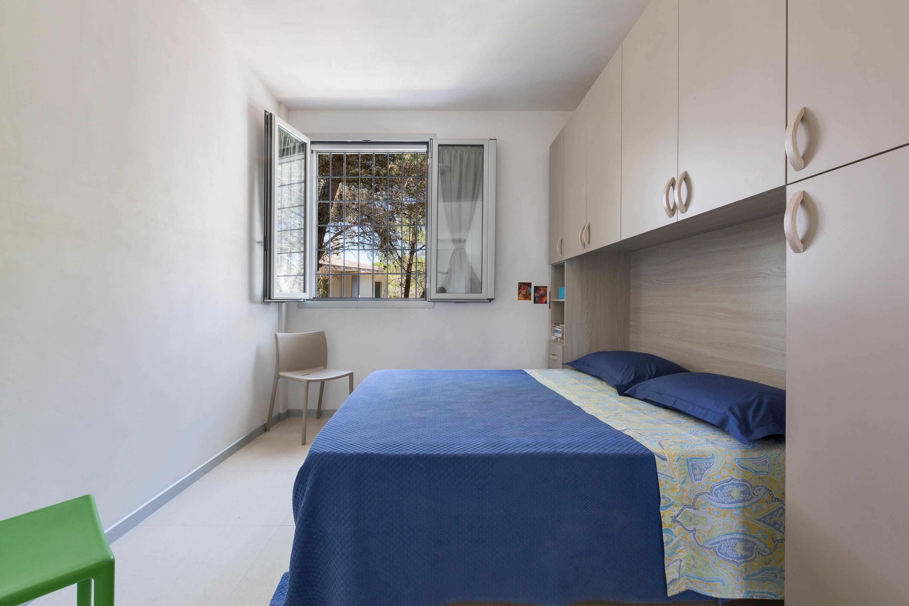 A bedroom with a bed, a chair, a window, and a wardrobe.