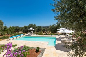 A swimming pool with lounge chairs and umbrellas, surrounded by olive trees and a clear sky. - Villa Sogno Bianco (Ostuni)