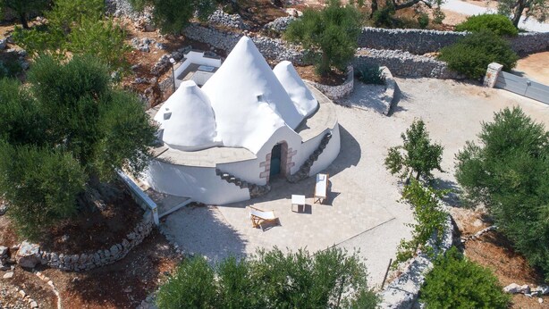 Un edificio blanco de forma abovedada con un camino de piedra que lo conduce, rodeado de árboles y un muro de piedra.